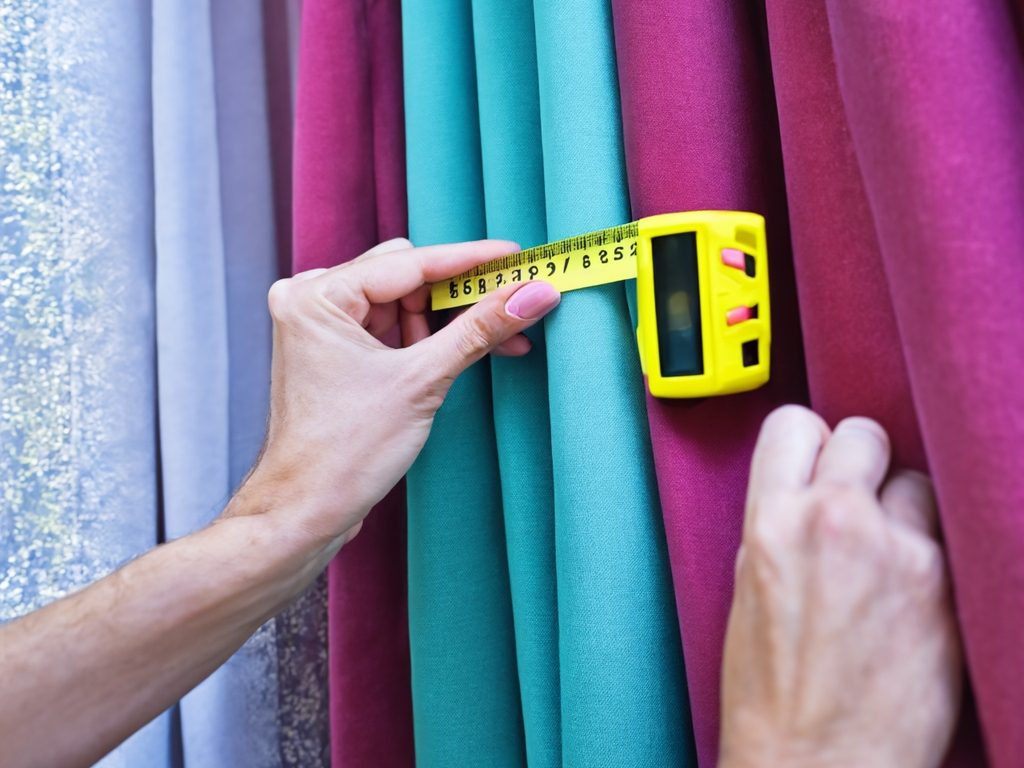 Main en train de mesurer des morceaux de tissu avec un mètre ruban jaune.